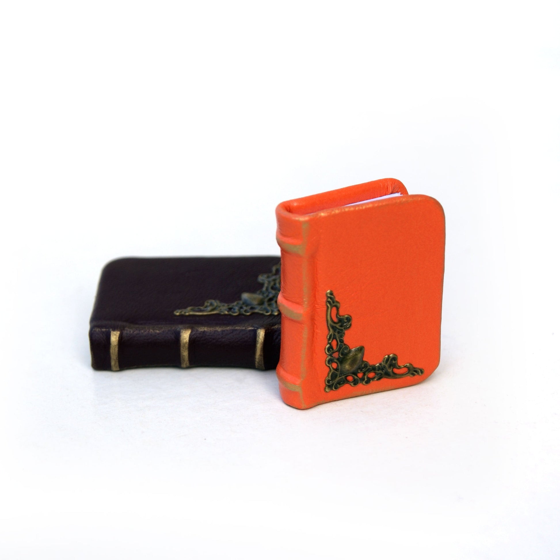 Two miniature books, one orange and one black with gold accents, on a white background.