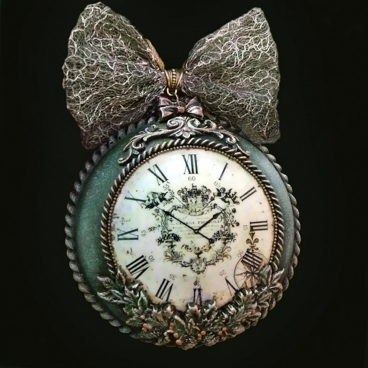 An antique-style decorative medallion- clock with a large textured gray bow on top, featuring a distressed green frame, Roman numerals, and a floral crest on the clock face.