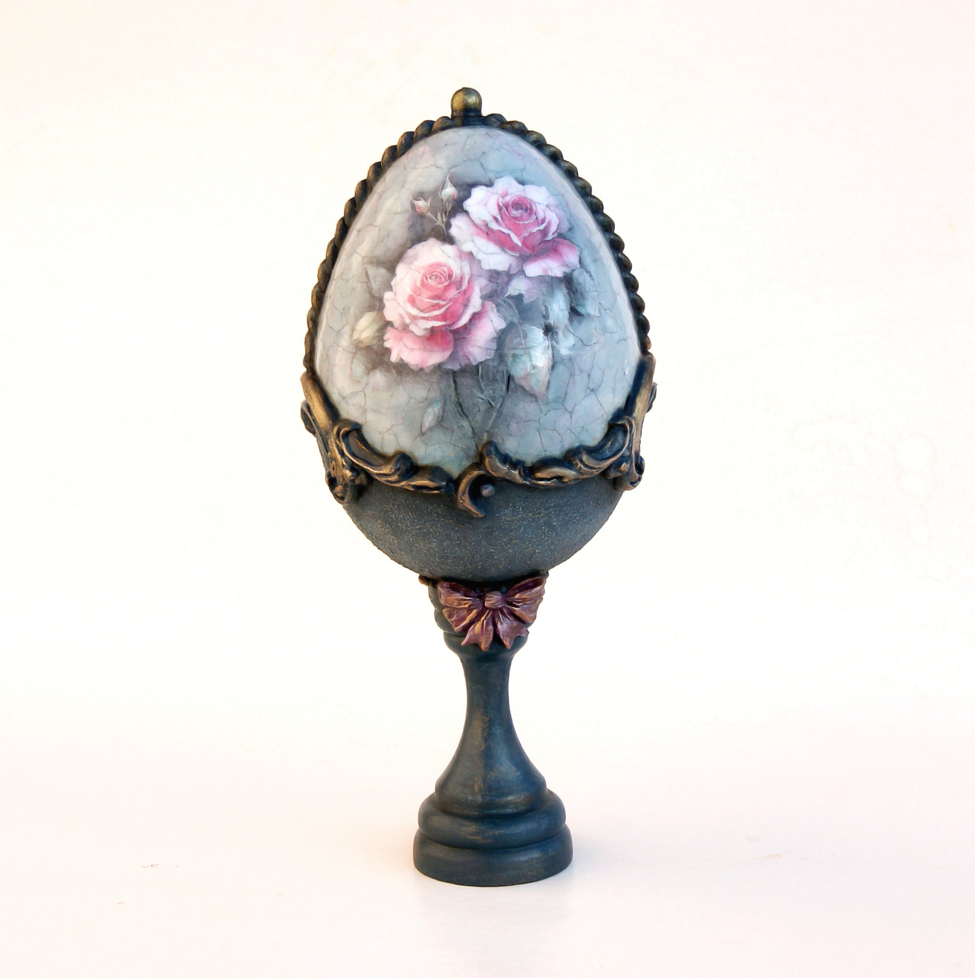 Decorative egg with floral design on a stand against a white background