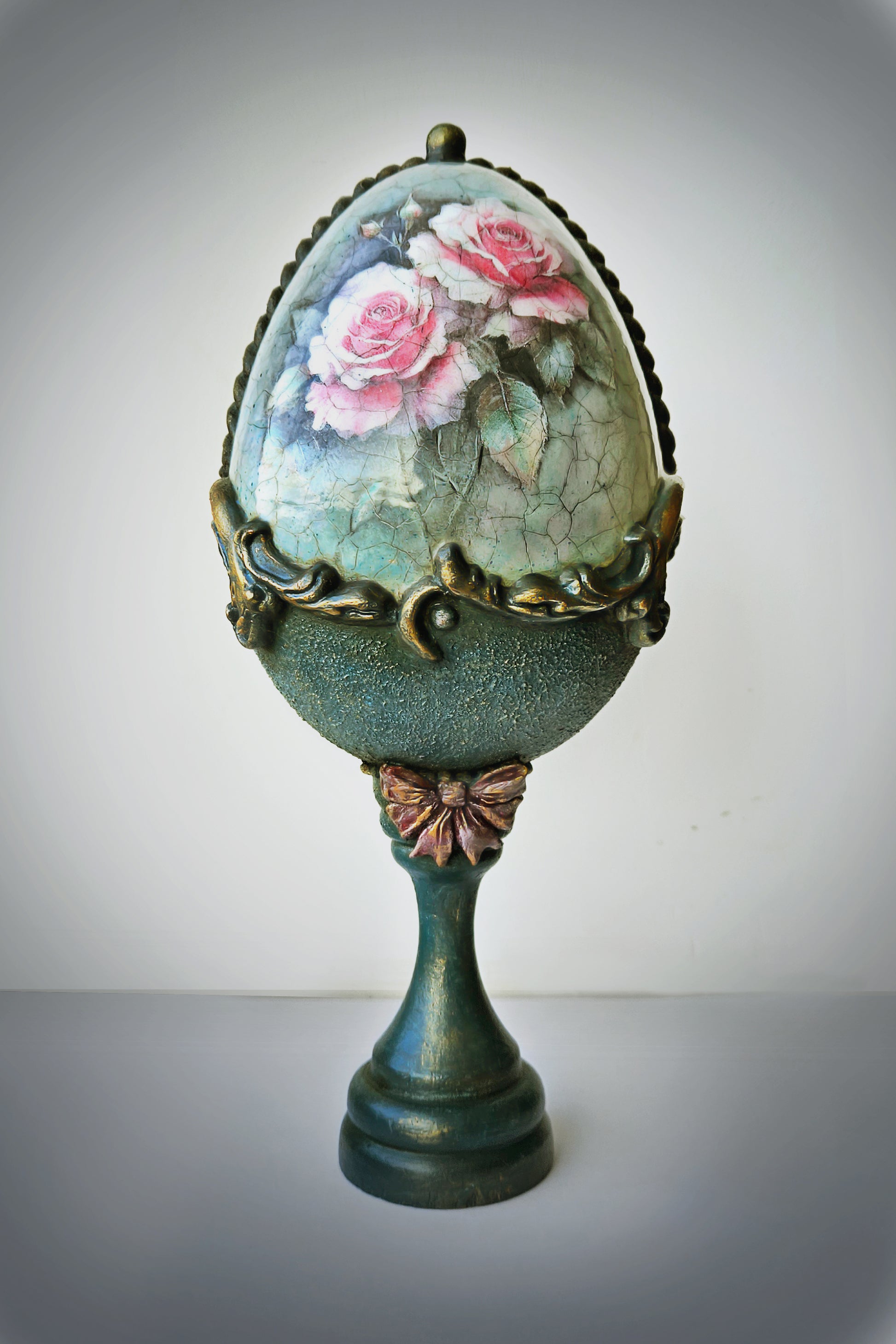 Decorative egg with floral design on a stand against a plain background