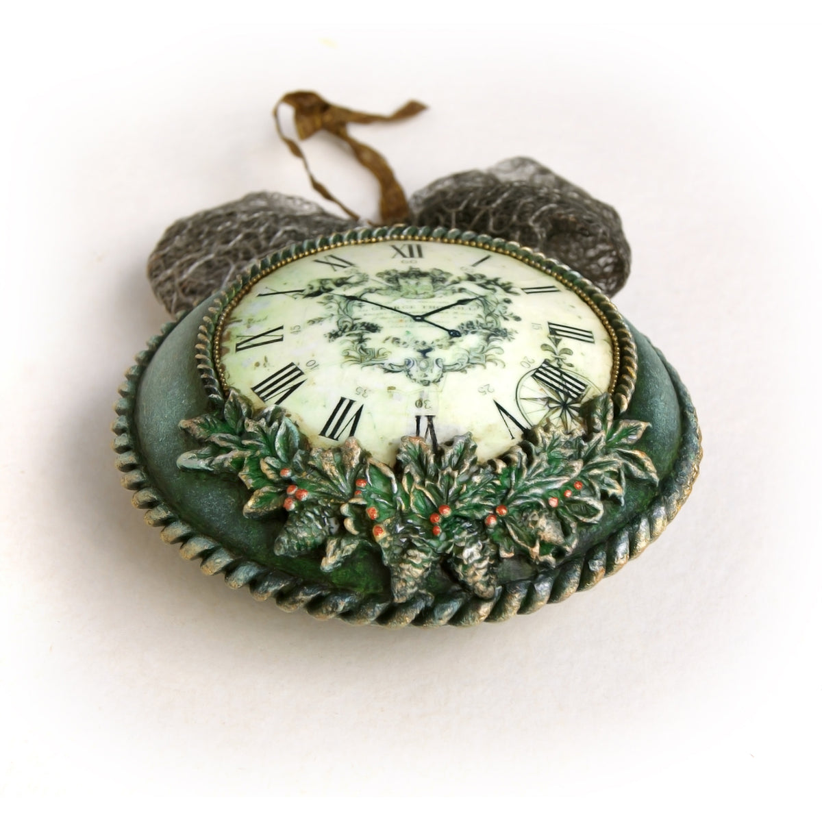 A decorative Christmas ornament shaped like a vintage clock, featuring a green body with a clock face, Roman numerals, holly leaves, and small red berries, with two hanging loops at the top, shown on a plain white background.